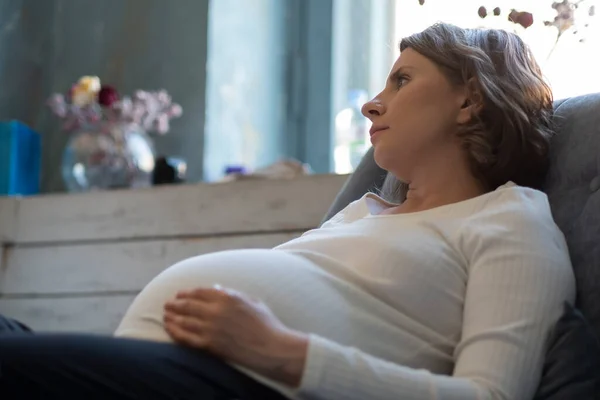 Mulher grávida no sofá olhando para longe sonhando. — Fotografia de Stock