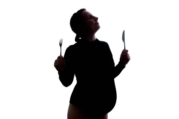 Joven embarazada comiendo sosteniendo tenedor y cuchillo sobre un fondo blanco. — Foto de Stock