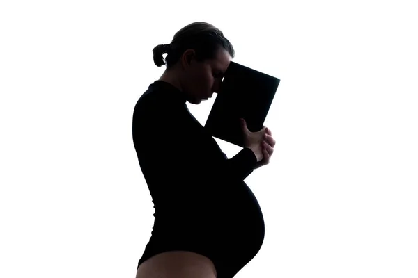 妊娠中の思慮深い女性の本を保持。シルエットビュー — ストック写真