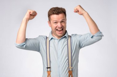 Gri arka planda yumruklarını kaldıran heyecanlı adamın portresi.