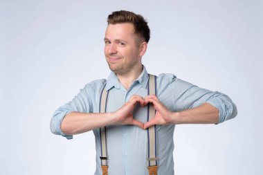 Gülümseyen genç adam göğsünde kalp hareketi yapıyor..