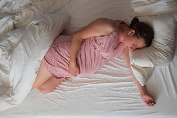 Durmiendo embarazada caucásica mujer en rosa ropa en la cama — Foto de Stock