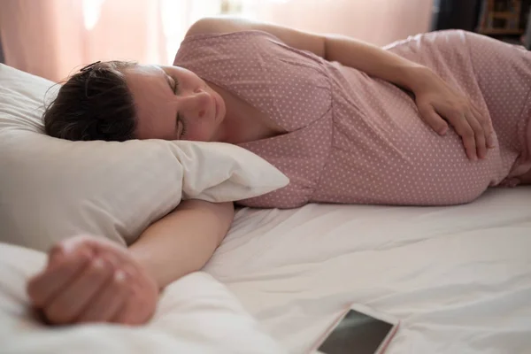 Спляча вагітна біла жінка в рожевому одязі на ліжку — стокове фото