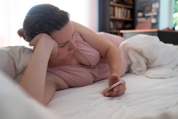 Беременная женщина лежит на кровати с сотовым телефоном — стоковое фото