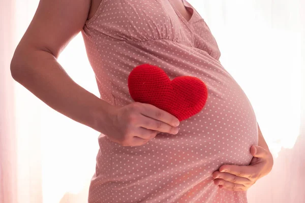 Mulher grávida com símbolo de coração vermelho segurando sua barriga — Fotografia de Stock