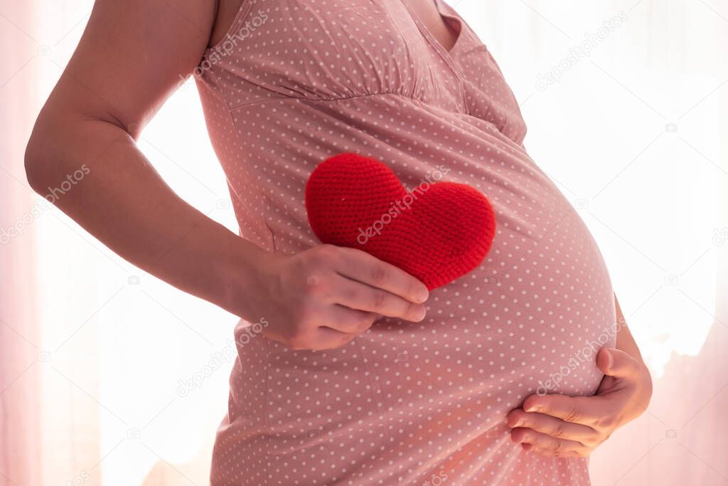 Pregnant woman with red heart symbol holding her belly