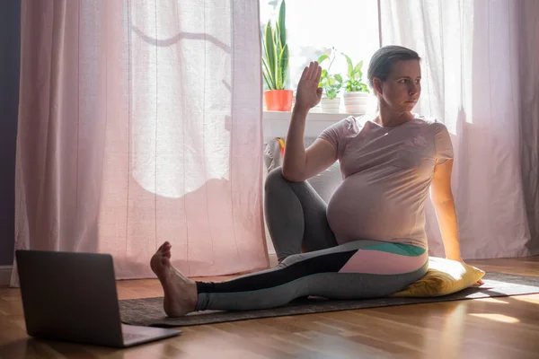 Pregnant woman sitting on floor stretching doing twisted asana — Stock Photo, Image