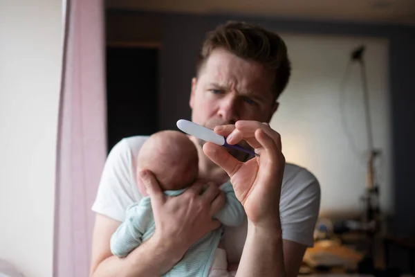 Worried oung father looking on thermometer holding his newborn baby in hands. — Stock Photo, Image