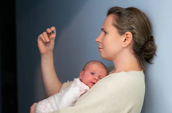 Aggódó anya nézi a hőmérőt, kezében az újszülött babájával.. — Stock Fotó