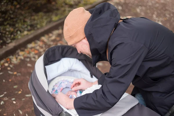 Щасливий молодий батько з коляскою перевіряє свою дитину під час прогулянки — стокове фото