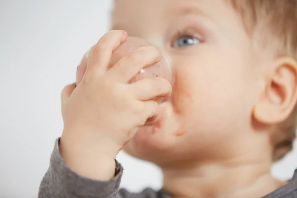 Cute little boy eating yogurt. Boy eating a fruit smoothie himself in the bedroom at the weekend , lazy morning, warm and cozy scene.