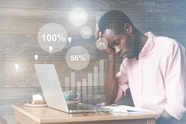 Overwork concept. African financial director working on a report, looking at the papers with frustrated and tired expression, resting his elbow on the table. Interest rates, percentage ratio interface