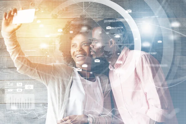 Double exposure of happy fashionable African girl with braces taking selfie via social network with mobile phone smiling at the camera while her boyfriend in glasses posing, kissing her in the cheek