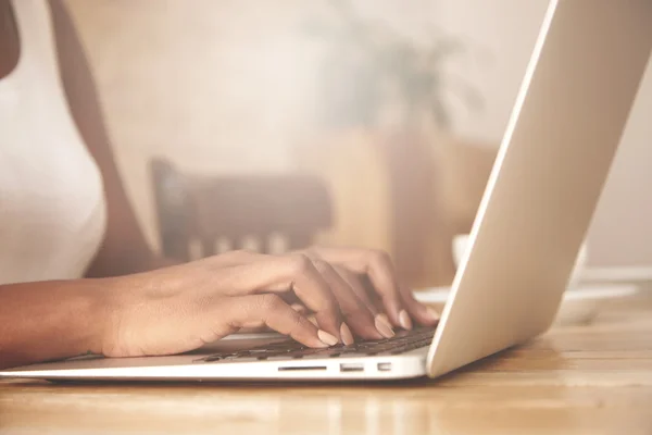 Cropped portrait of African female blogger keyboarding on laptop computer, posting a new article on her blog. Busy woman hand typing on keyboard while sitting at her working place in the office