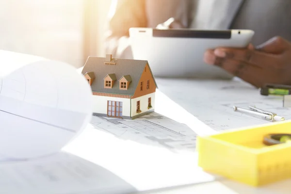 Architecture, building and construction. Cropped shot of African architect holding digital tablet, working on new real estate project, sitting at desk with engineering tools and scale model house