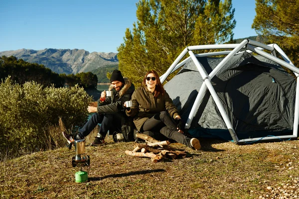 Couple camping drinking coffee near tent smiling happy outdoors