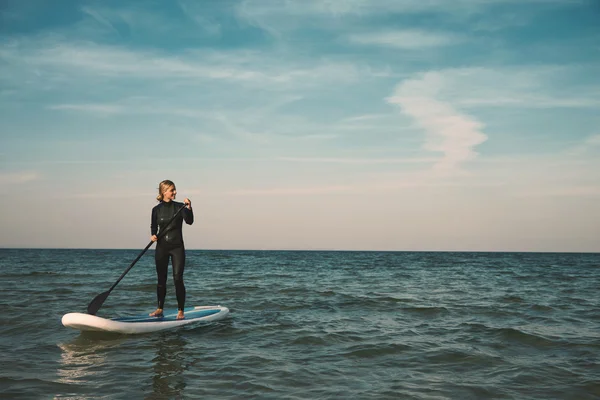 Young blonde female paddles a paddleboard at the sea.