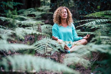 Rahatlamış güzel bayan meditasyon yapıyor. Doğa bitkisinin ortasında oturuyor. 