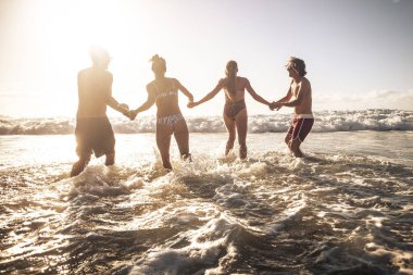 Bir grup arkadaş, altın bir günbatımında deniz suyunda birlikte plajda yaz tatilinin tadını çıkarıyorlar.