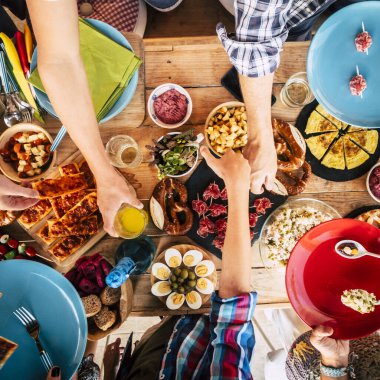 Bir grup arkadaşın, yemek dolu ahşap bir masada birlikte yemek yemesini dikey görüyorum. 