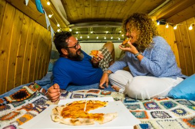 Çift içeride pizza yerken eğleniyor. Alternatif yaşam tarzında ahşap minibüs yapımı el yapımı. Seyahat tatili. 