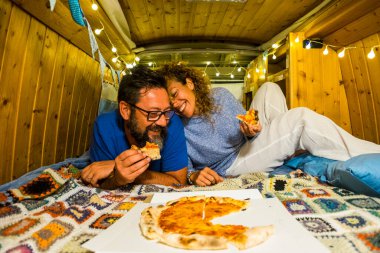 Çift içeride pizza yerken eğleniyor. Alternatif yaşam tarzında ahşap minibüs yapımı el yapımı. Seyahat tatili.