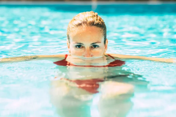 Portrait of woman with face down the water at the pool and eyes outside looking at the camera