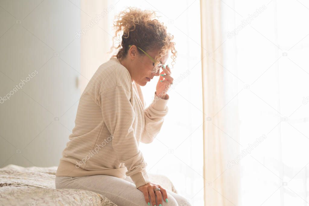 Woman suffering from stress or a headache grimacing in pain sitting on the bed in bedroom at home in morning with her other hand to her nose