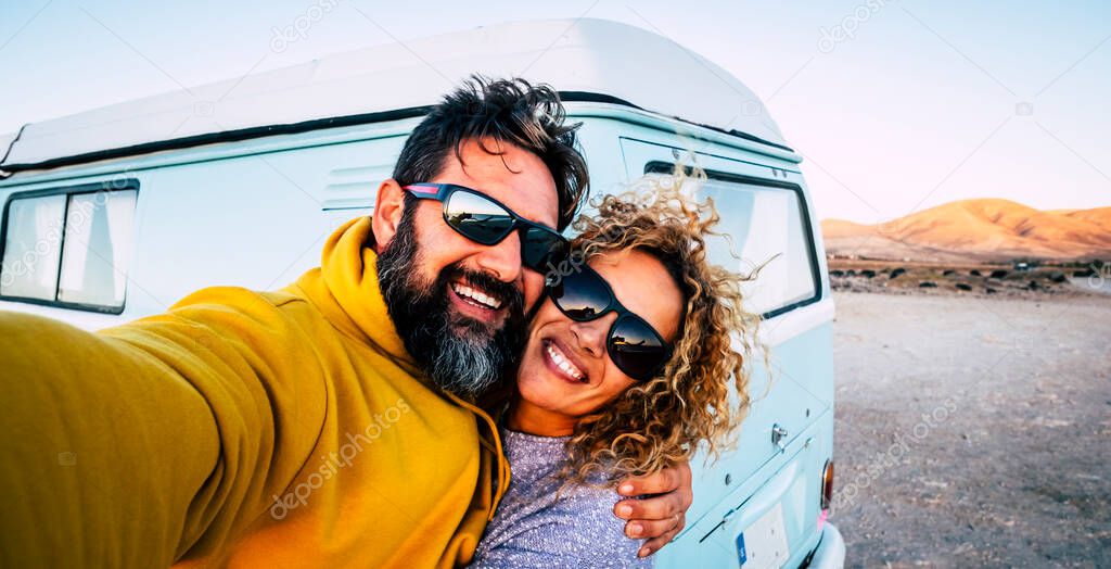 Happy adult couple smile and have fun together taking selfie picture with old vintage classic van in background 