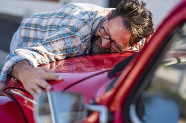 Yakışıklı sakallı adam yeni arabasına sarılıyor ve gülümsüyor.