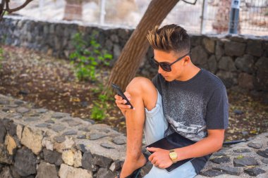 Beyaz çocuk bahçenin dışında cep telefonu kullanıyor. Oturuyor ve dinleniyor.