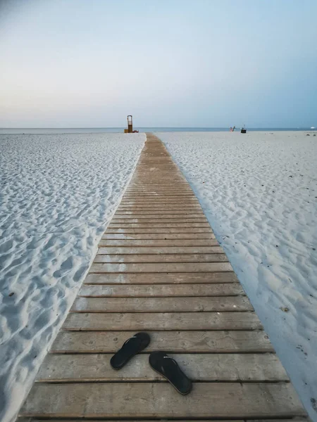 Długa Drewniana Ścieżka Białej Plaży Piasek Wody Morskiej Parą Sandałów — Zdjęcie stockowe