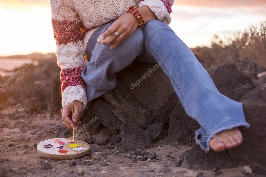 Cropped shot of barefoot woman painting while sitting on rocks
