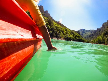 Kadın gezgin, kanyonda kayık sürüşünün keyfini çıkarırken, arka planda el altından suya ve dağa batıyor.