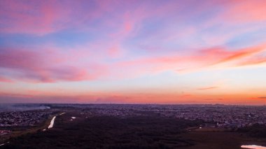 Vanilya gökyüzü ve pembe ve mor renkli bulutlarla gün batımının hava aracı görüntüsü. Tüm şehrin tabanında.