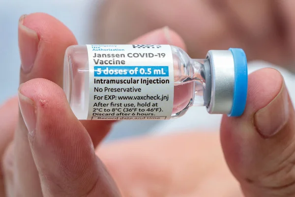 Vial of Covid-19 vaccine manufactured by Janssen laboratory held by fingertips