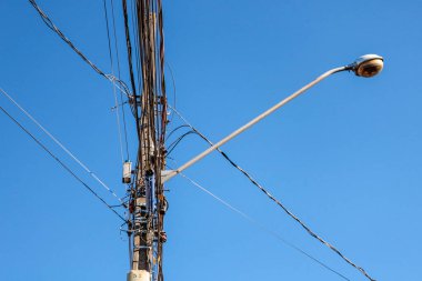 Sokak lambası direği. Kabloların karışıklığı ve mavi gökyüzü vurgulanıyor.