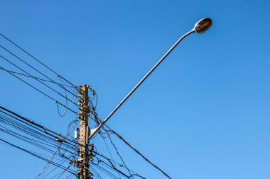 Sokak lambası direği. Kabloların karışıklığı ve mavi gökyüzü vurgulanıyor.