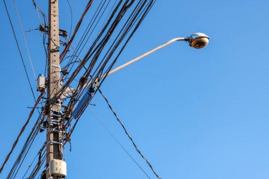 Sokak lambası direği. Kabloların karışıklığı ve mavi gökyüzü vurgulanıyor.