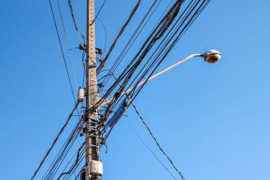 Sokak lambası direği. Kabloların karışıklığı ve mavi gökyüzü vurgulanıyor.