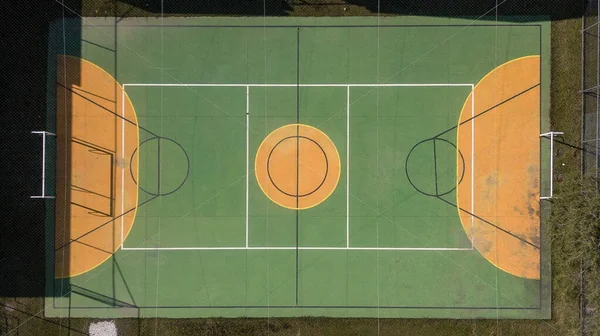 Multi-sport court (volleyball, futsal and basketball), in green and yellow, covered with net and a little dirty due to the weather.