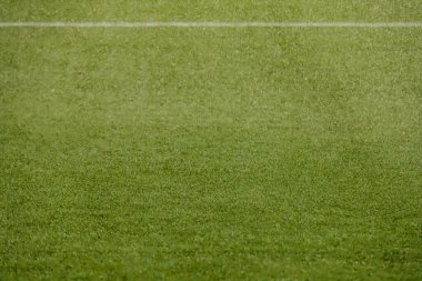 Üzerinde sentetik çimenler olan futbol sahası beyaz bir çizgiyle ıslanıyor.