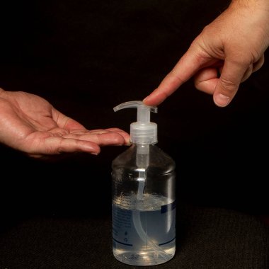 Siyah arka planda, erkek eli ellerini temizleyebilmek için alkol jeliyle bir kap açar.