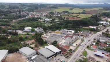 Campo Magro şehrinin hava manzarası, ana yolu, evleri, ticari binaları ve sanayi bölgelerini gösteriyor. Sahne, bulutlu bir günde bitki örtüsü, tarla ve tepelerle çevrilidir..