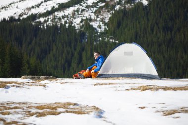 Bir çadır ve bir sırt çantası yakınında oturan turist.