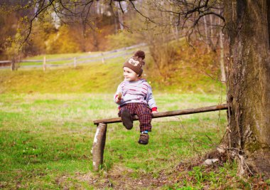 Küçük bir çocuk bir ağacın altında oturuyor.