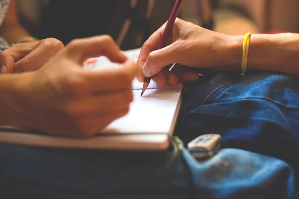 A person draws with a pencil in a notebook.