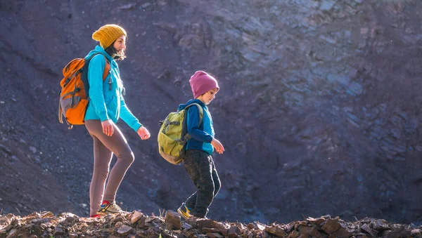 A woman is traveling with a child. Mom and son in the mountains. Climb to the top of the mountain with children. The boy with the backpack climbed to the top. Active vacations.