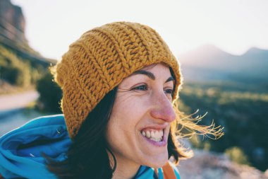 Sırt çantasıyla dağların arkasında gülümseyen bir kızın portresi. Türkiye 'de seyahat. Örgü şapkalı bir kadın bir dağın tepesinde duruyor..