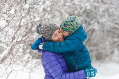 Çocuk annesine sarılıyor. Annesiyle kış yürüyüşüne çıkmış bir çocuk. Örgü şapkalı bir çocuk annesini öper. Kadın oğlunu destekliyor. Annelik. Aile birlikte zaman geçirir. Aile değerleri.